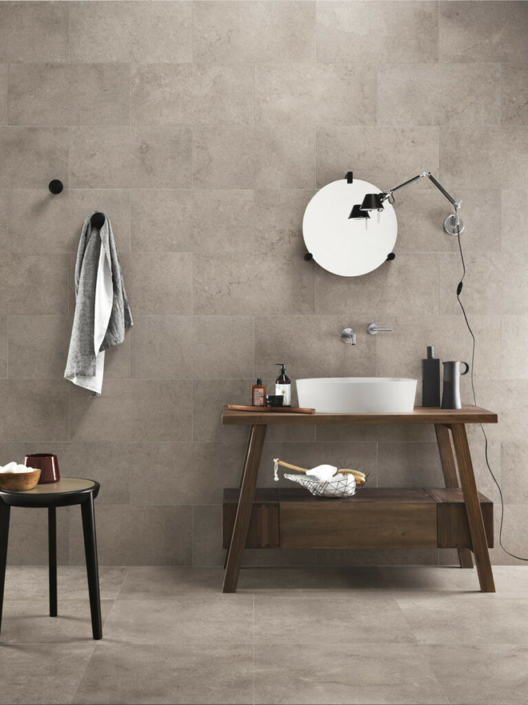 Zona de aseo diario con lavabo sobre mueble de madera y superficies soladas y alicatadas con piedra porcelánica gris en dos formatos, cuadrado y rectangualr