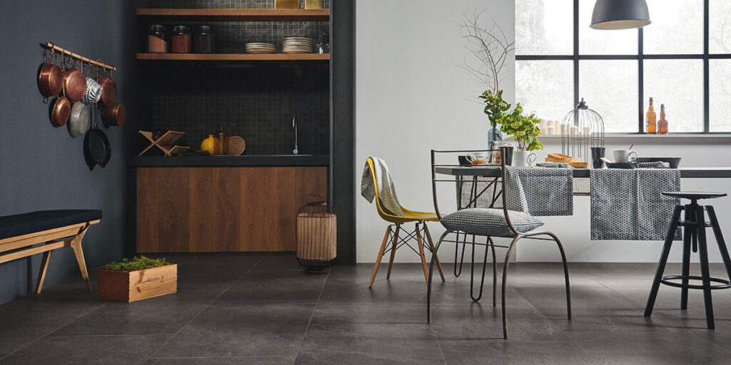 Zona comedor en cocina con tonos grises y un pequeño toque rompedor en amarillo en la que destaca el suelo en piedra porcelánica en color gris oscuro y acabado mate.