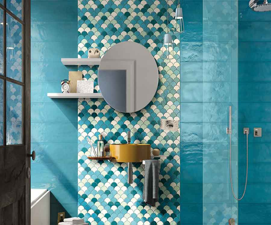 Colorido baño que combina en la pared frontal un lienzo de azulejo de escamas en tonos azules con franjas a ambos lados de baldosa porcelánica de superficie irregular en color azul turquesa