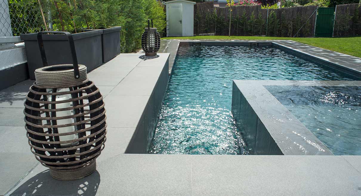 Primer plano de zona de spa en piscina con interior y exterior revestido con porcelánico efecto piedra natural en color gris