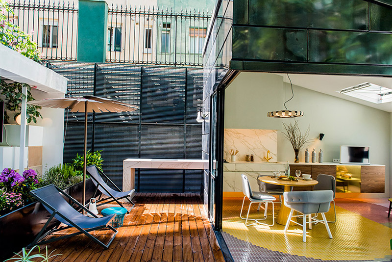 Perspectiva desde el exterior de la zona de estar y comedor integrada en la cocina y la encantadora terraza ambas con solado en madera porcelánica