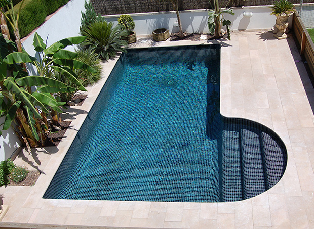 Patio interior con piscina revestida con mosaico azul y zona de playa en piedra porcelánica